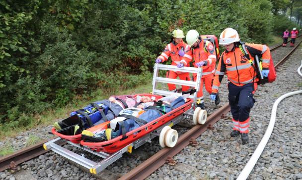 Drei Personen von Rettungsdiensten schieben eine Trage auf einer Schiene.