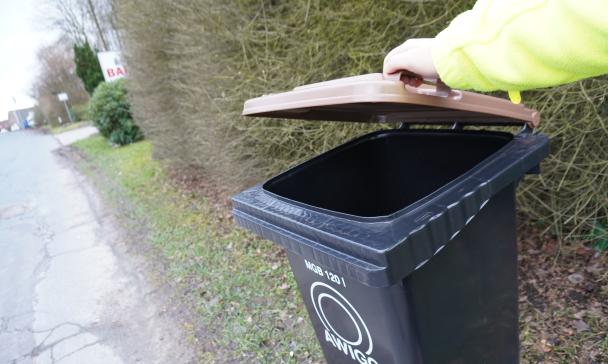 Person hebt den braunen Deckel einer Abfalltonne an.