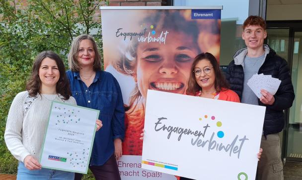 Vier Personen stehen neben einem Rollup-Poster.