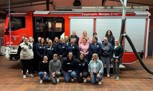 Eine Personengruppe steht vor einem Feuerwehrauto.