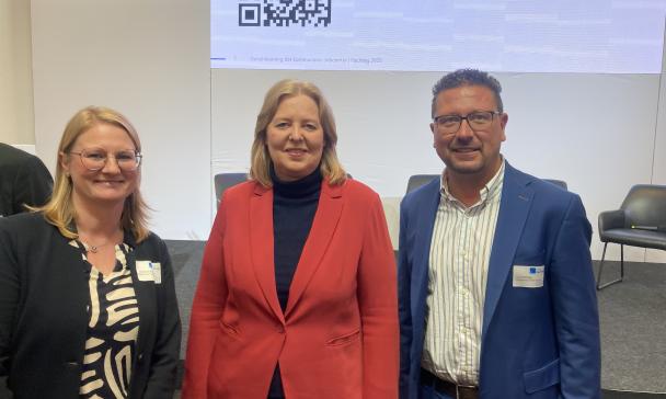 Drei Personen vor Plakat