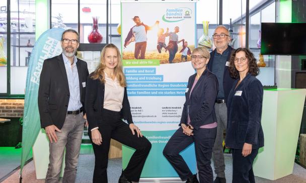 Fünf Personen stehen neben einem Rollup-Poster.