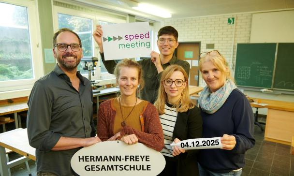 Fünf Personen stehen in einem Klassenraum.