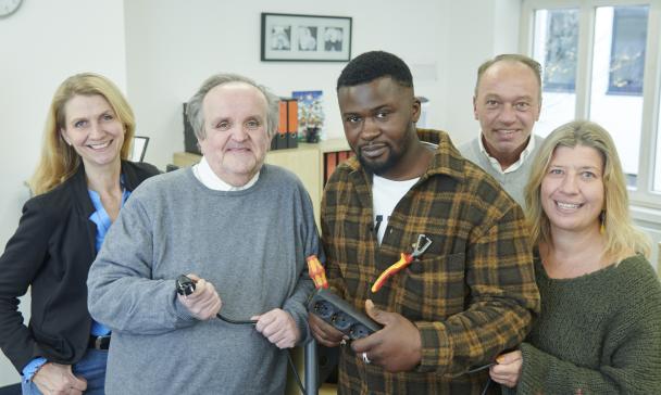 Fünf Personen mit Steckerleiste in den Händen stehen in einem Büro.
