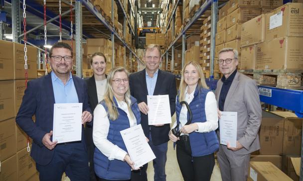 Sechs Personen stehen in einem Hochregallager.