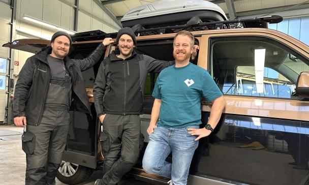 Drei Personen stehen vor einem Wohnmobil in einer Werkhalle.