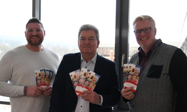 Drei Personen Stehen im Gegenlicht vor einer Glasfassade.