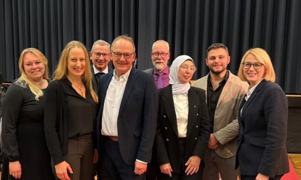 Eine Personengruppe steht vor einem Vorhang.