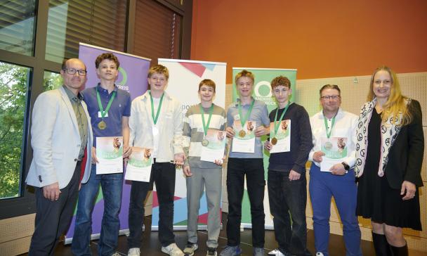 Personengruppe mit Medaillen und Urkunden steht vor Rollup Postern