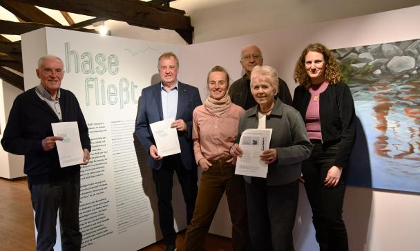 Sechs Personen stehen in einer Ausstellung nebeneinander.