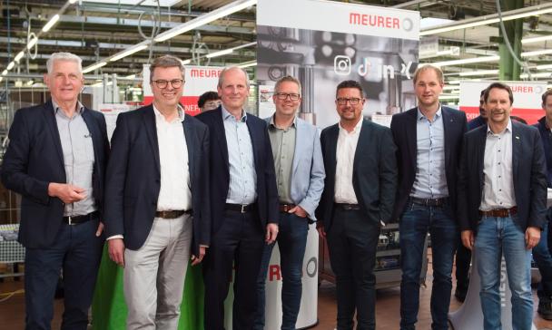 Sieben Personen stehen in einer Werkhalle.