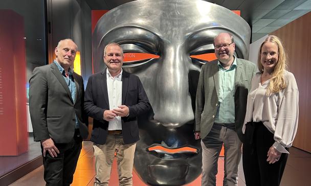 Vier Personen vor einer übergroßen römischen Maske
