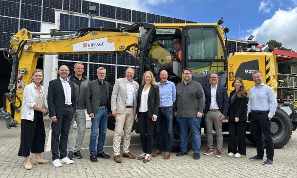 Personengruppe vor einem Bagger auf einem Hof